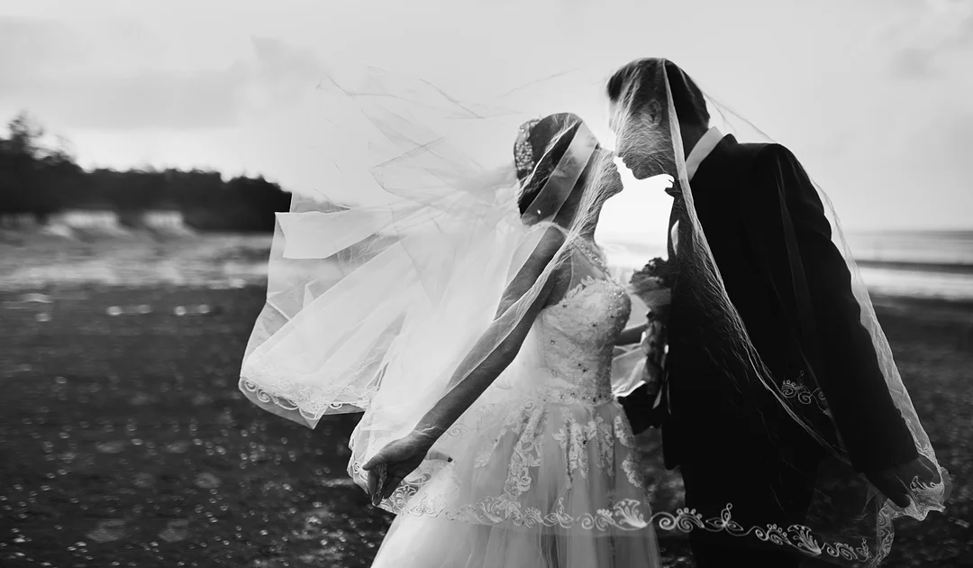 Black and white photo of a couple kissing behind a windblown veil